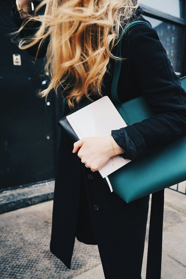 Femme aux cheveux longs avec carnet et sac vert – mobilité et assurance éco-responsable